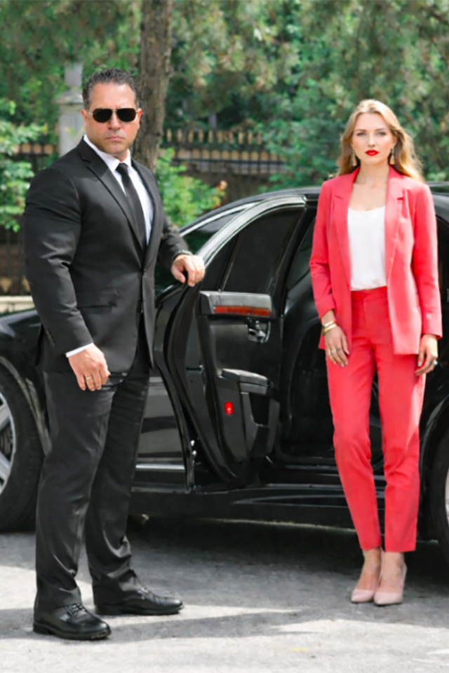 A professional security officer in a clean white uniform and cap, holding a walkie-talkie and looking alert while on duty. The uniform features a 'Security' gold embroidery and an official Guardion Protection badge.